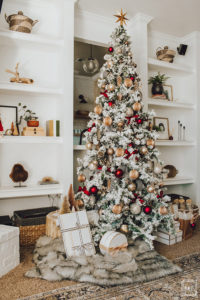 Warm and Cozy Christmas tree with pink, burgundy and gold ornaments, black and white stripe ribbon, satin burgundy ribbon tied in bows, brass tree collar, glittered magnolia leaves, faux fur west elm throw blanket and white + gold Christmas gifts add the perfect touch to these custom living room built-ins.