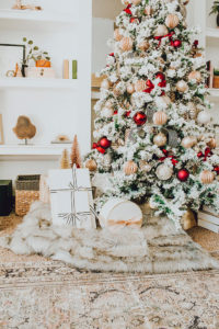 Warm and Cozy Christmas tree with pink, burgundy and gold ornaments, black and white stripe ribbon, satin burgundy ribbon tied in bows, brass tree collar, glittered magnolia leaves, faux fur west elm throw blanket and white + gold Christmas gifts add the perfect touch to these custom living room built-ins.