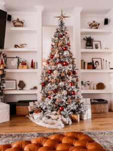 BURGUNDY AND GOLD CHRISTMAS DECORATING IDEAS | Living room decorated for Christmas with a Flocked Christmas tree, burgundy, gold, and silver ornaments, and a fireplace mantle decorated with flocked garland, bottle brush trees, large gold bells, and cream stockings.