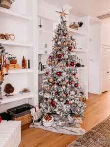 BURGUNDY AND GOLD CHRISTMAS DECORATING IDEAS | Living room decorated for Christmas with a Flocked Christmas tree, burgundy, gold, and silver ornaments, and a fireplace mantle decorated with flocked garland, bottle brush trees, large gold bells, and cream stockings.